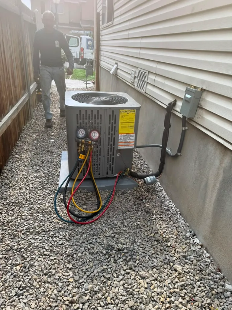 Lucas Heating and Air technician commissioning a newly installed air conditioner with gauges connected in a narrow side yard