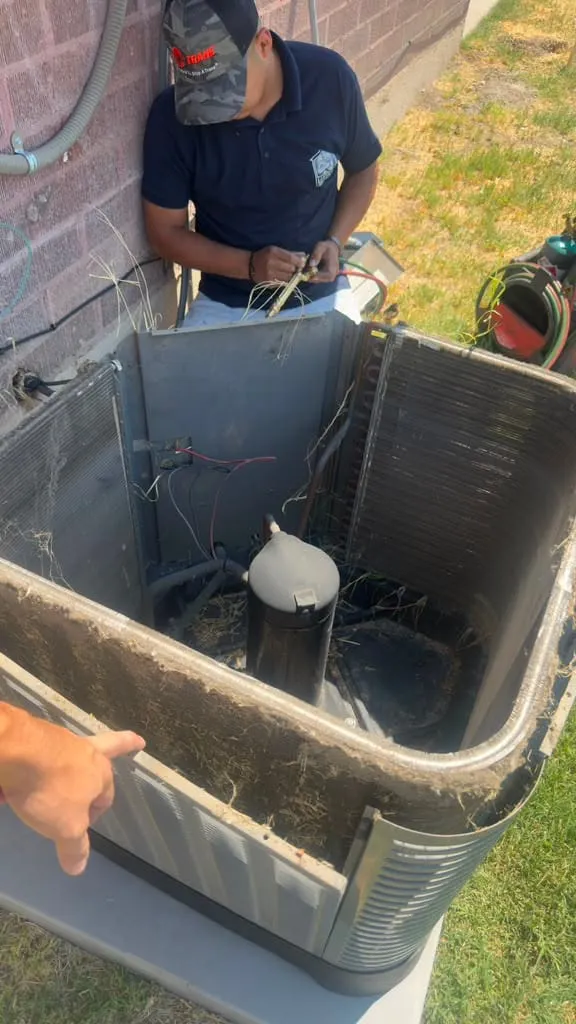 Lucas Heating and Air technician cleaning debris out of an opened AC condenser during a tune-up in Salt Lake City's Rose Park neighborhood