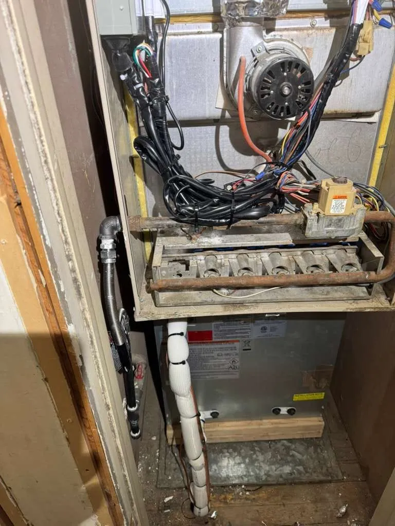 Older downflow furnace opened for repair by Lucas Heating and Air, showing the inducer motor, burner rack, and gas valve in a utility closet