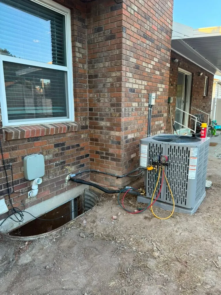 New AC condenser installed by Lucas Heating and Air at the corner of a brick home in Bountiful, gauges still connected for commissioning
