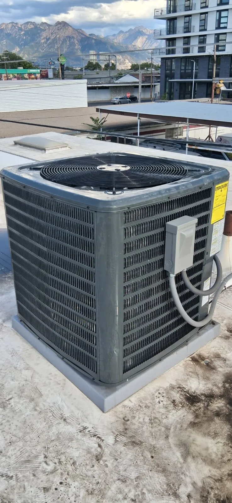 New AC condenser on a Salt Lake City rooftop serviced by Lucas Heating and Air, with the Wasatch Range behind it